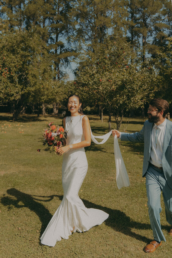 Stu helping carry Eura’s veil across the lawn before the ceremony, a playful and candid backyard wedding moment.