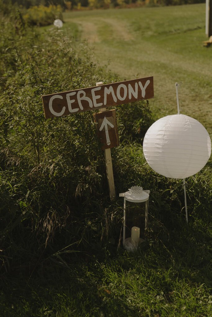 Wooden ceremony sign along the grassy path leading guests to the outdoor ceremony site, a rustic backyard wedding detail.