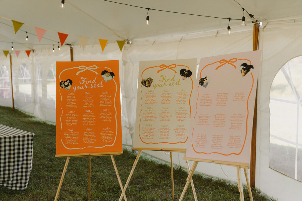 Colorful seating charts displayed on easels under the sailcloth tent at this backyard wedding, a bright and creative garden wedding party idea.
