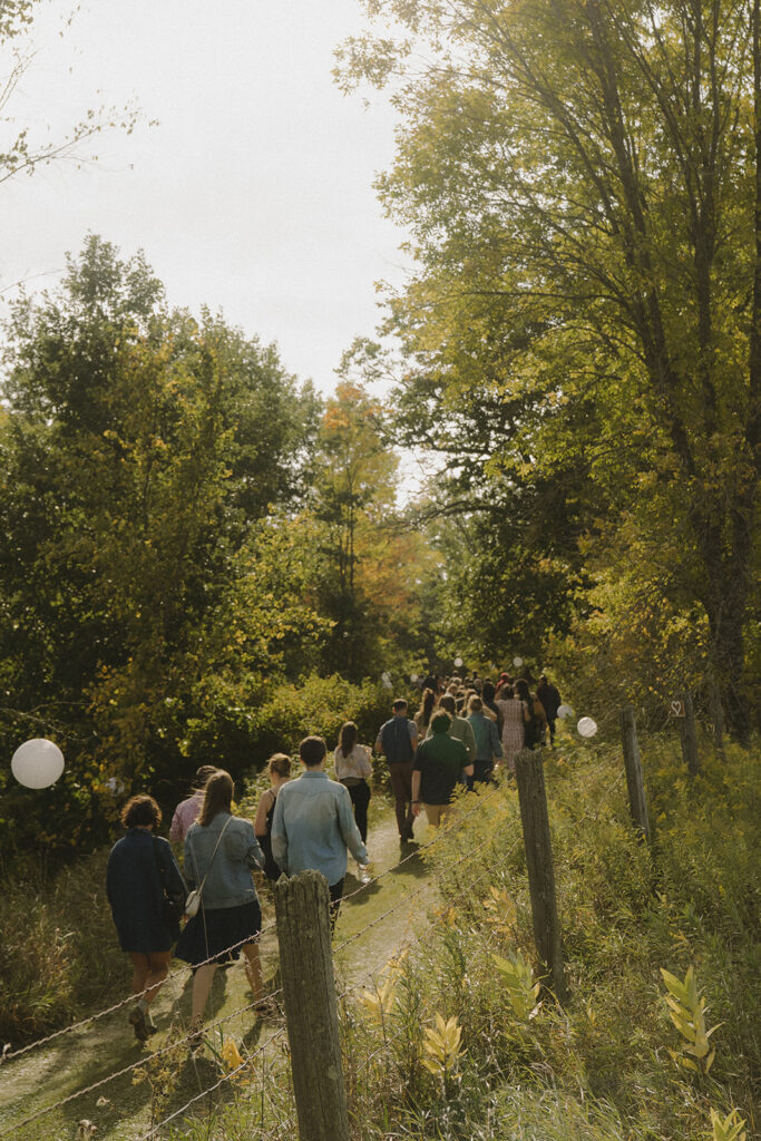 Guests walking up the wooded trail to the hilltop ceremony, a unique garden wedding party entrance through the trees.