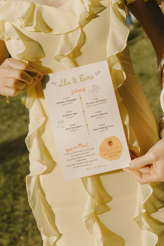 Guest holding the illustrated wedding program during Eura and Stu’s backyard wedding, showing playful design details and garden party styling.