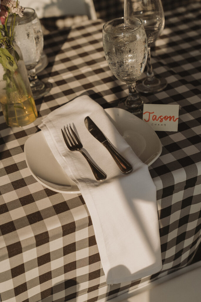 Backyard wedding tablescape with gingham linens, real dishware, and handwritten place cards, an elevated approach to outdoor wedding reception styling.