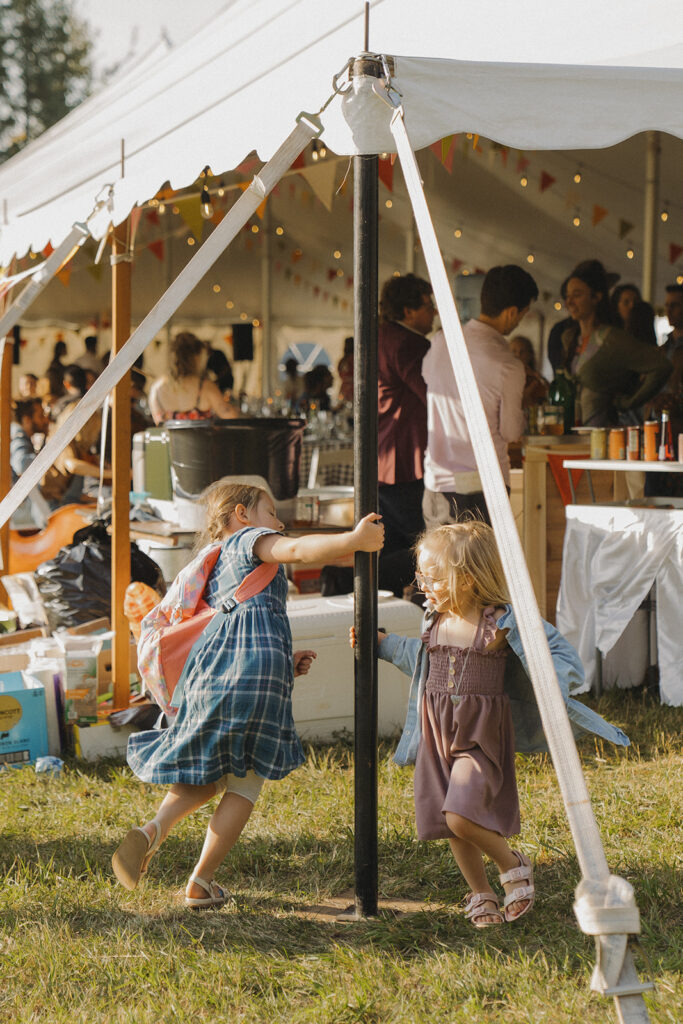Kids running and playing beside the sailcloth tent during cocktail hour, capturing the laid-back, family-centered feel of this backyard wedding celebration.