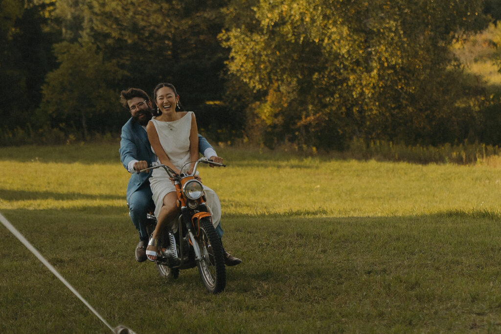 Eura and Stu riding a vintage dirt bike across the lawn for their backyard wedding entrance, a fun and unexpected reception idea.