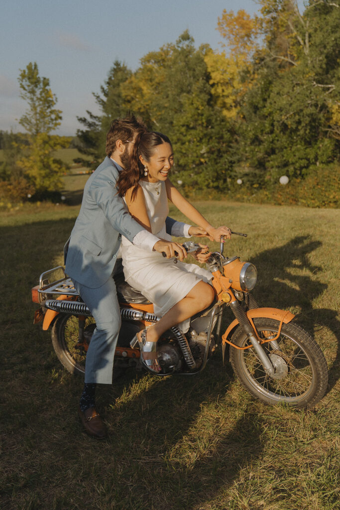 Stu driving the dirt bike with Eura smiling on the back, a playful backyard wedding photo taken before the reception.