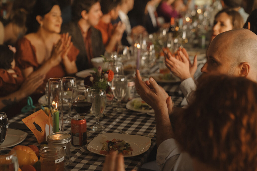 Guests clapping during heartfelt toasts at the backyard wedding reception, with candles and produce-inspired décor lining the tables.