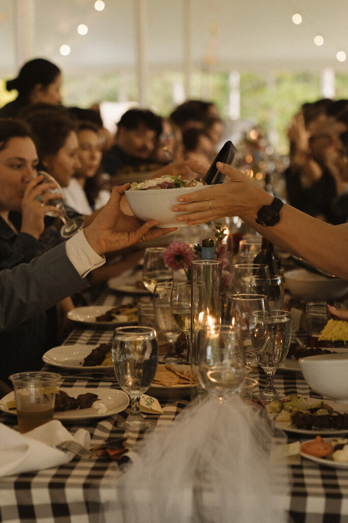 Guests passing bowls of food family style during Eura and Stu’s backyard wedding reception, a relaxed dinner idea for outdoor weddings.