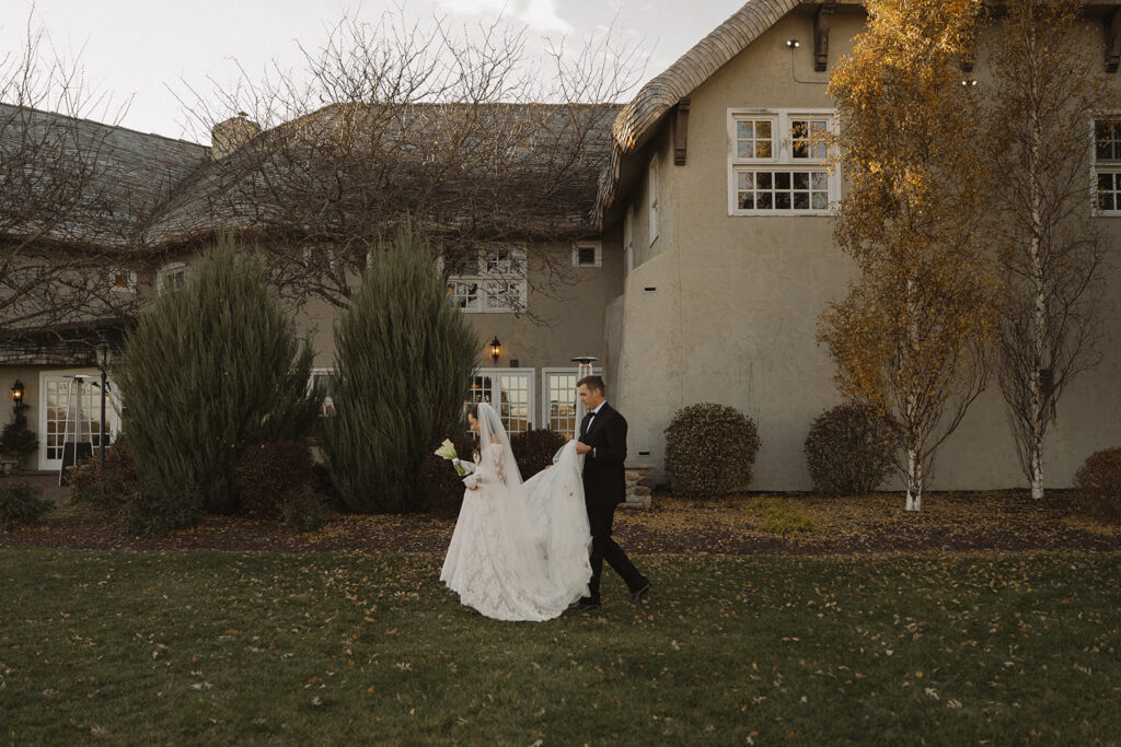 Groom trails behind bride holding her train as they make their way across the grounds of Edward Anne Estate before their vintage wedding