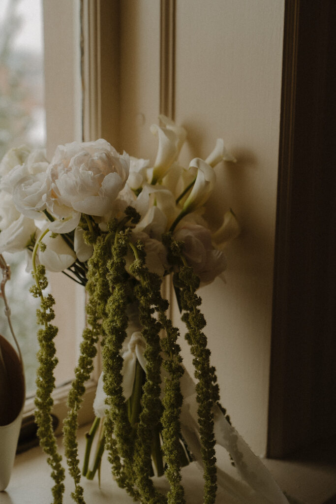 White lilies and roses of bridal bouquet sit propped in the windowsill 