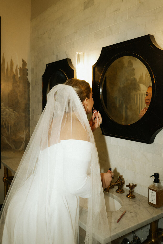 Bride touches up her lip gloss in the mirror at Semple Mansion historic wedding venue in Saint Paul, MN