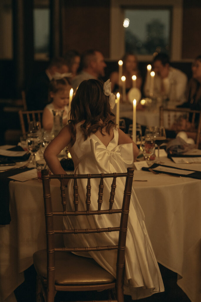 Flower girl crawls up to the table at candlelit wedding reception