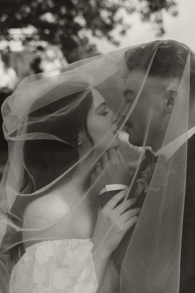 Bride and groom lean in for a kiss under the cover of bride's veil in vintage wedding pics