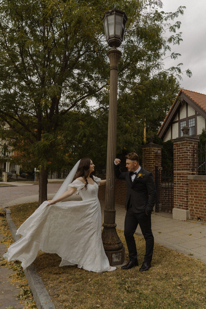 Groom leans against lamppost and admires his bride while she twirls around