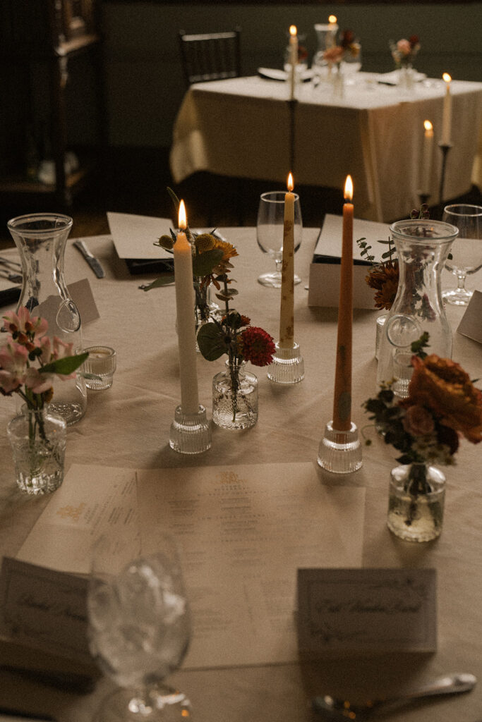 Tablescape adorned with multi color taper candles and sprays of flowers in bud vases
