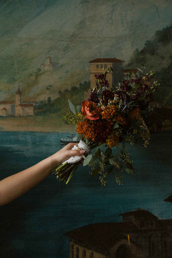 Bride holds up her colorful wedding bouquet against backdrop of Italian painting at WA Frost and Company