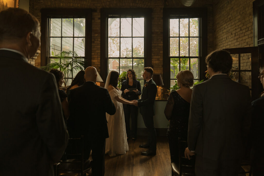 Bride and groom stand in front of their friends and family at vintage wedding ceremony at WA Frost and Company in Semple Hill, Saint Paul, MN.