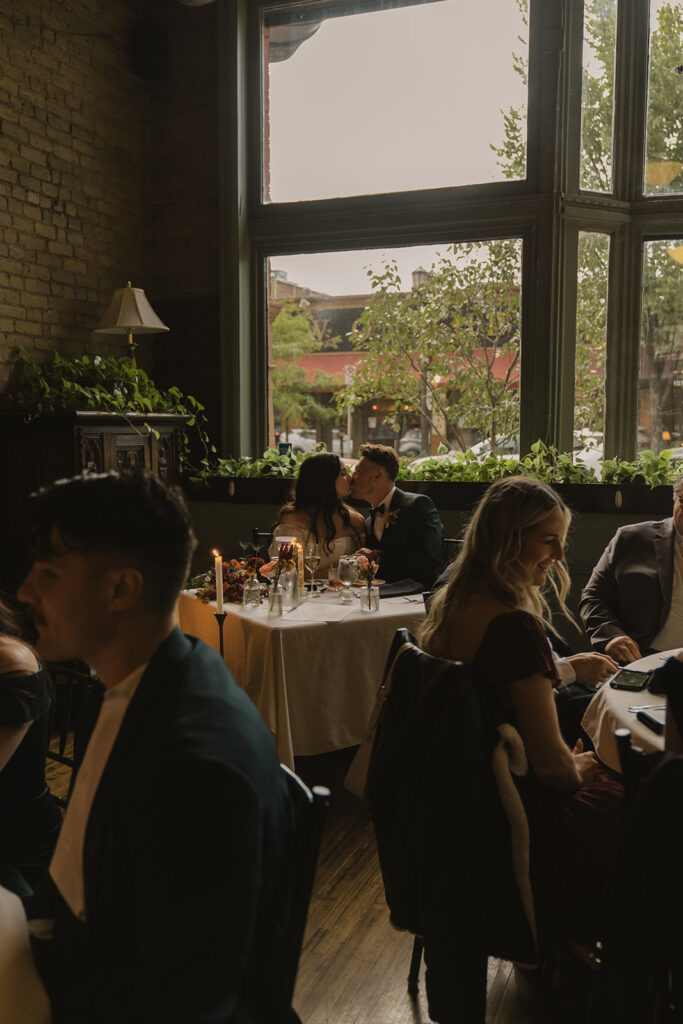 Bride and groom kiss at sweetheart table during their vintage wedding reception at WA Frost and Co. in Saint Paul, Minnesota