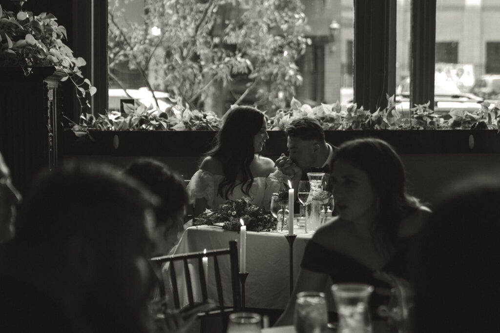 Groom kisses bride's hand in private moment at sweetheart table during vintage wedding reception