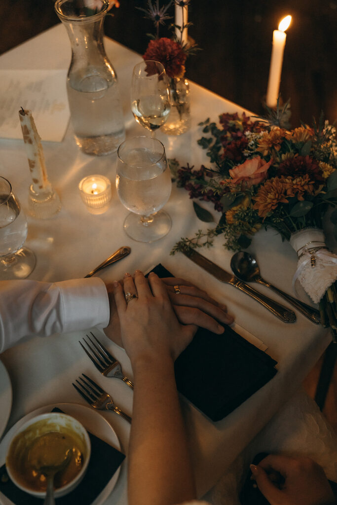 Bride and groom hold hands at sweetheart table covered with taper candles and autumnal florals