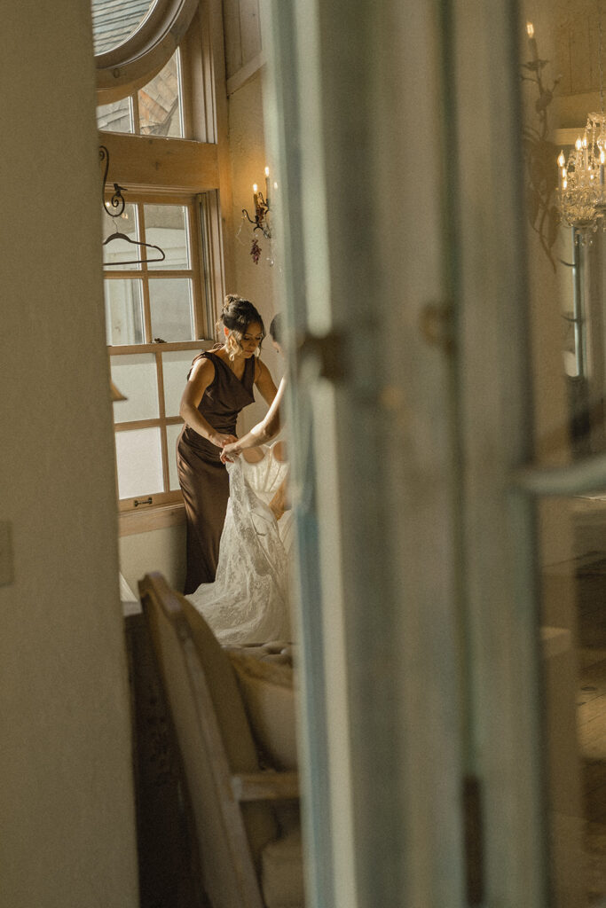 Bridesmaid helps bride get into her vintage wedding dress at Edward Anne Estate