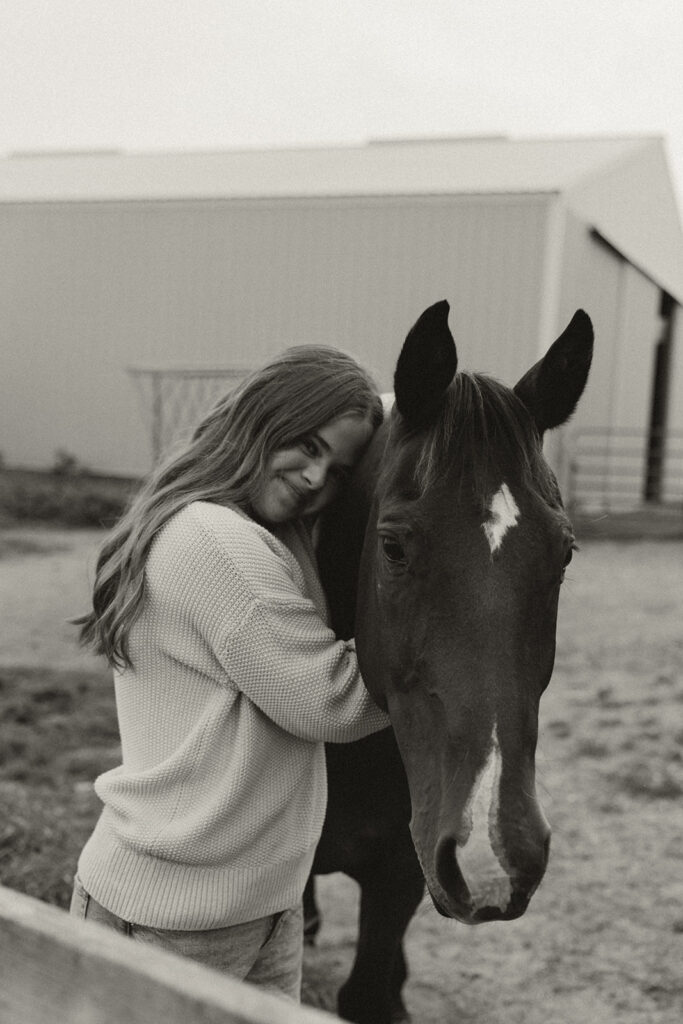 Senior pic inspiration of young girl hugging her horse with the Minnesota stables behind them