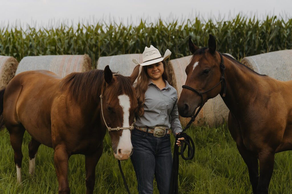 Minnesota senior photos of young cowgirl holding two horses in a field
