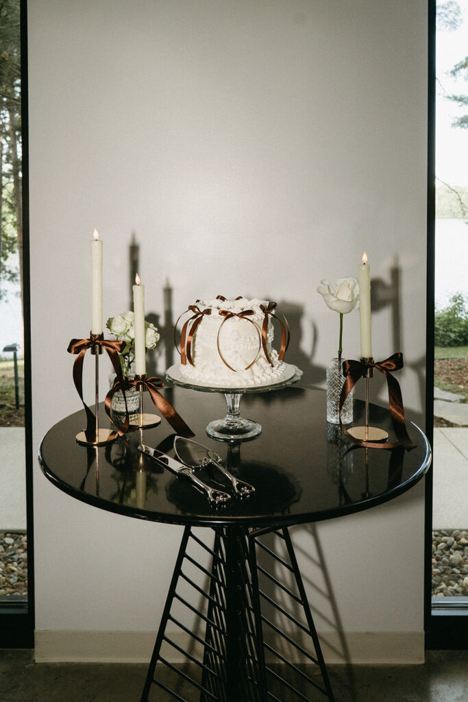Vintage wedding cake topper of brown bows on classic white cake, surrounded by taper candles and white roses