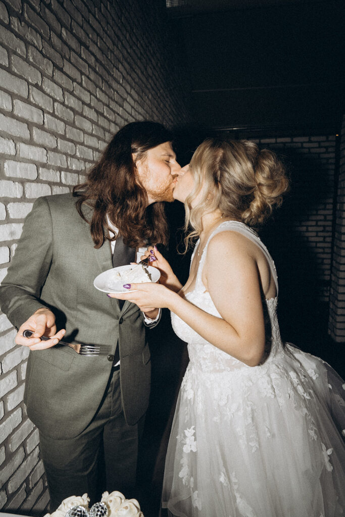 Bride and groom kiss over a plate of wedding cake