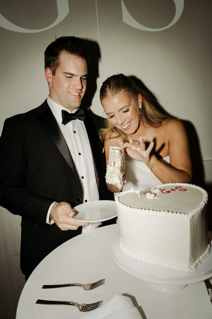 Bride balances a slice of cake on a cake server while her husband waits with an empty plate