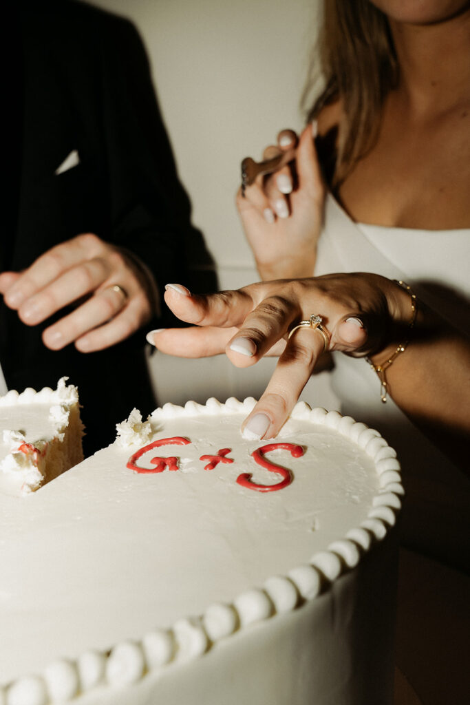 Bride scrapes some frosting off of their initialed, heart-shaped vintage wedding cake