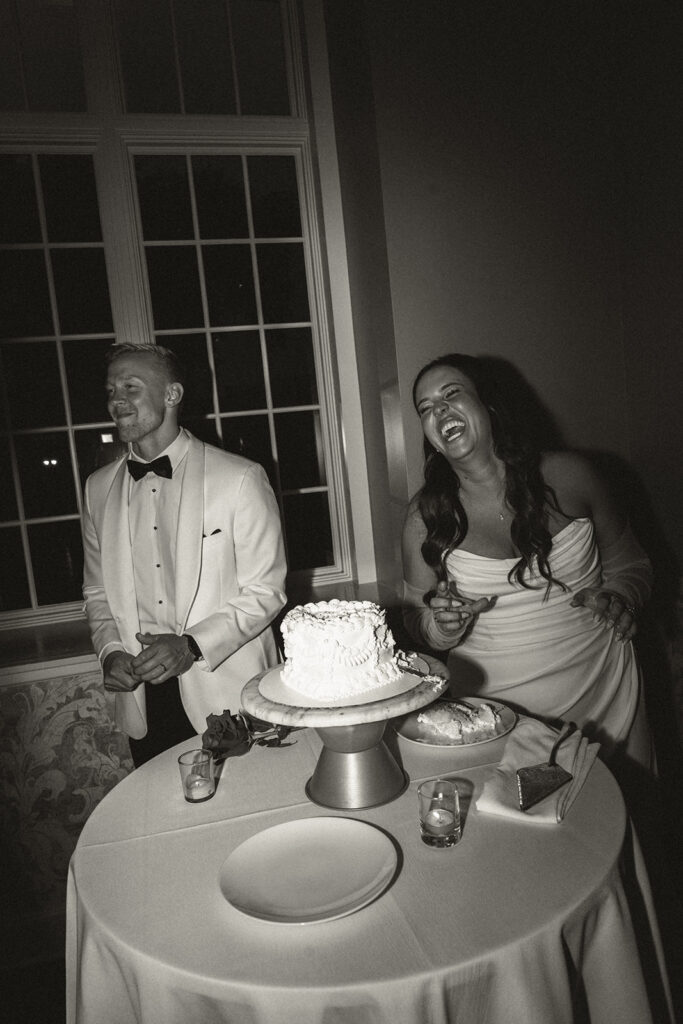 Bride and groom laugh in playful moment during wedding cake pictures