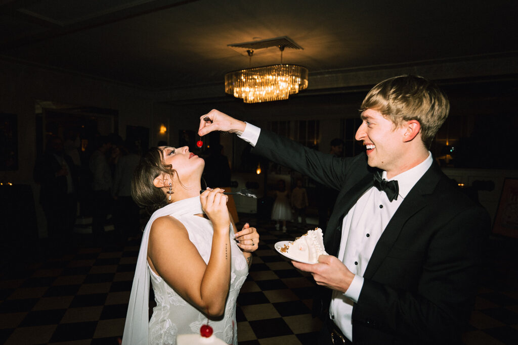 Groom feeds bride a cherry in playful, candid portrait at historic wedding venue in Saint Paul, Minnesota