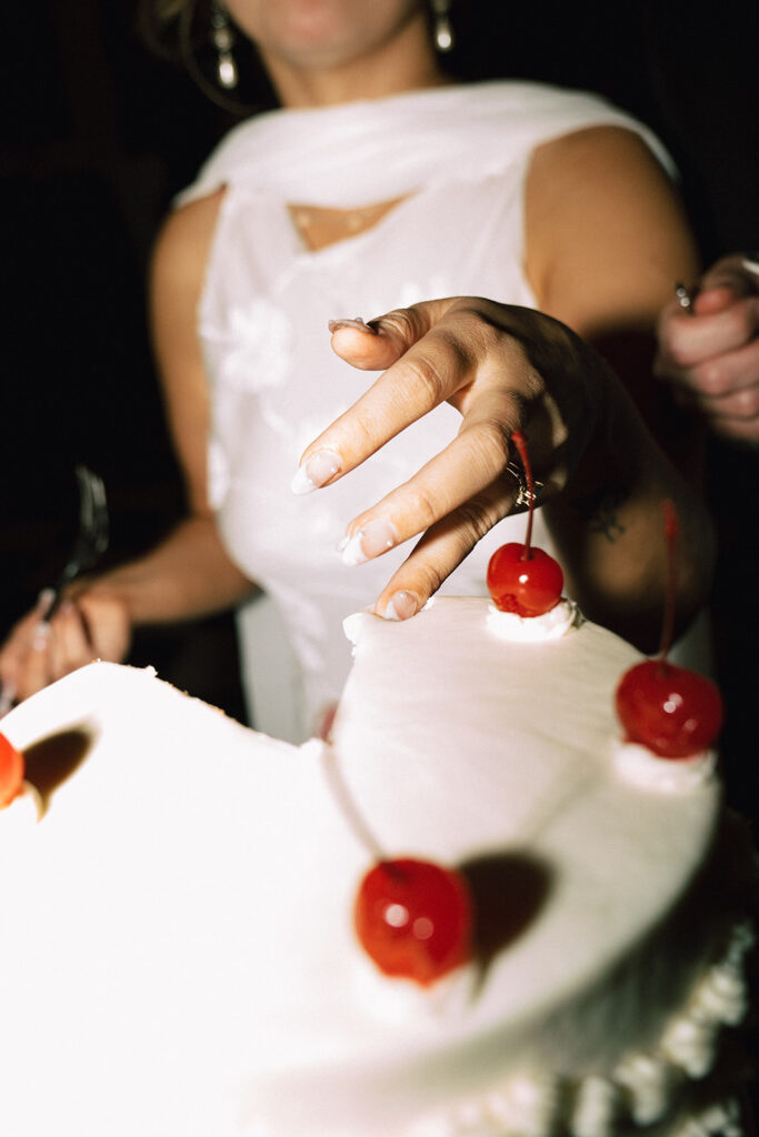 Bride scrapes some white frosting off the top of the cake, narrowly missing a cherry.