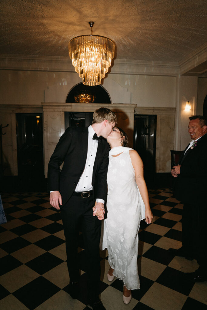 Bride and groom kiss as they walk across black and white tile of historic wedding venue in Saint Paul, Minnesota