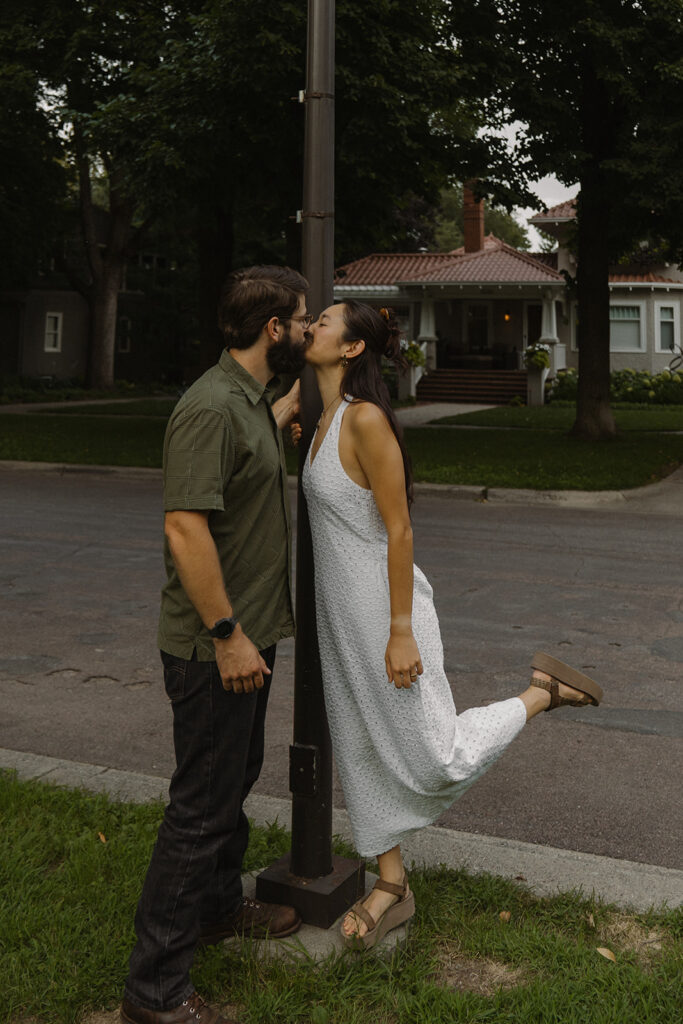 Couple kisses beneath a streetlamp while she lifts one foot, offering fun couple photoshoot ideas inspired by classic 90s rom com movie scenes.
