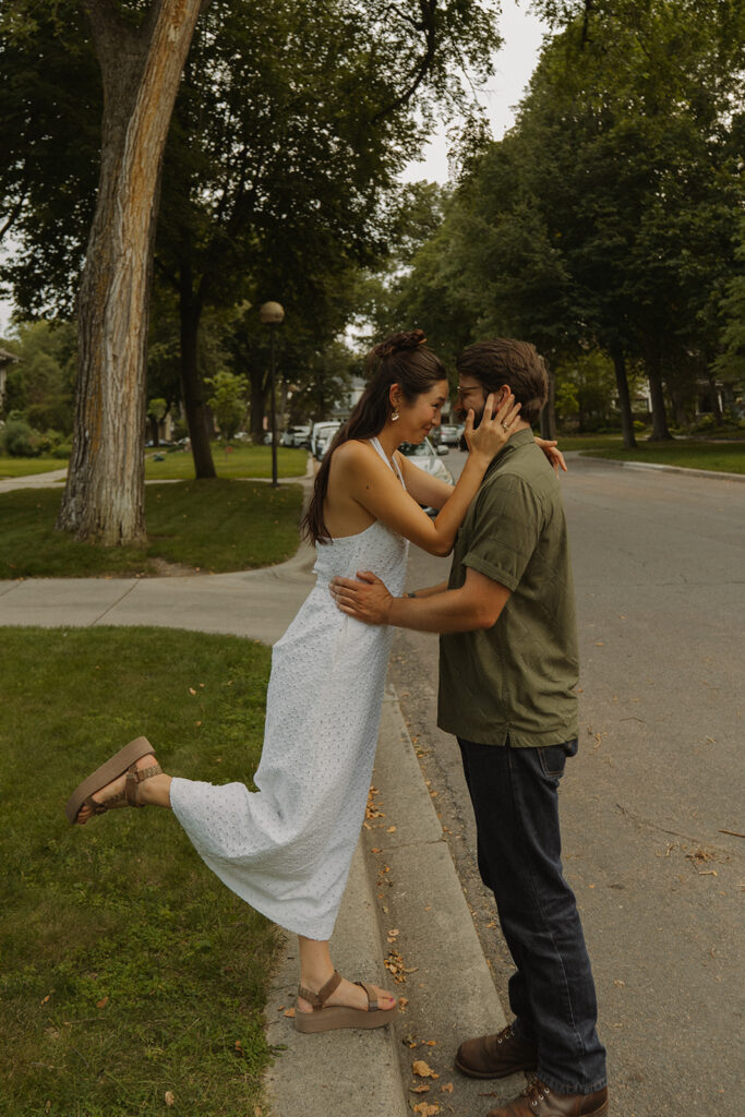 Couple embraces on a quiet residential street while she lifts one leg, inspired by classic 90s rom com movie moments and fun couple photoshoot ideas.