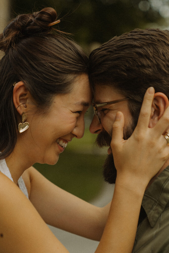 Close-up of couple touching foreheads and laughing together, capturing intimate vintage engagement photos with warm Nancy Meyers aesthetic emotion.