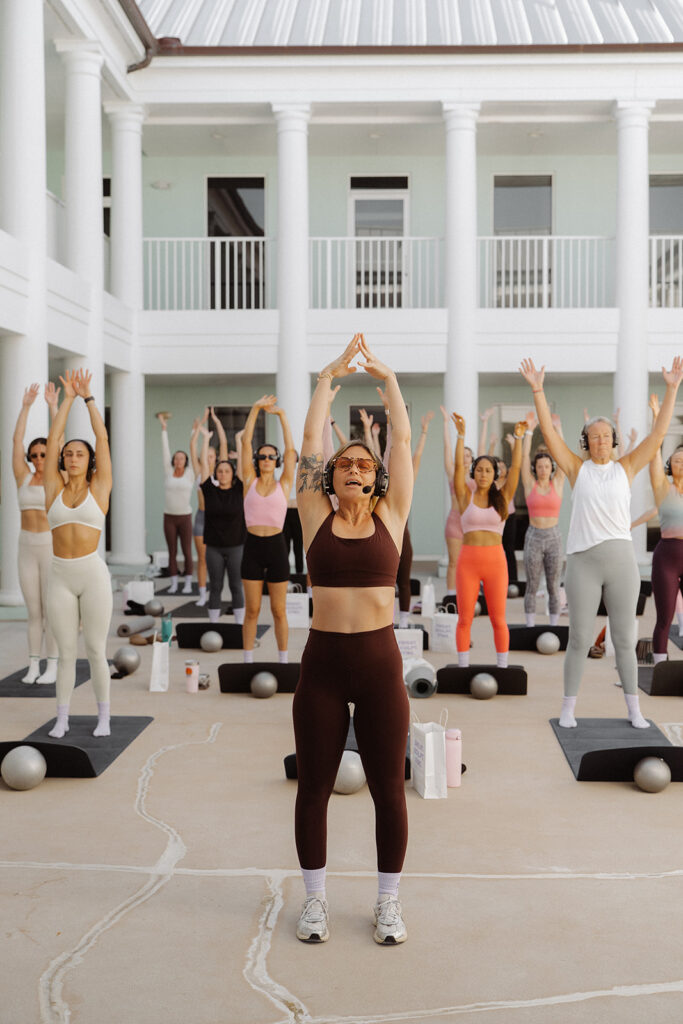 Instructor leading outdoor workout class with crowd behind her, event branding photos full of motion.