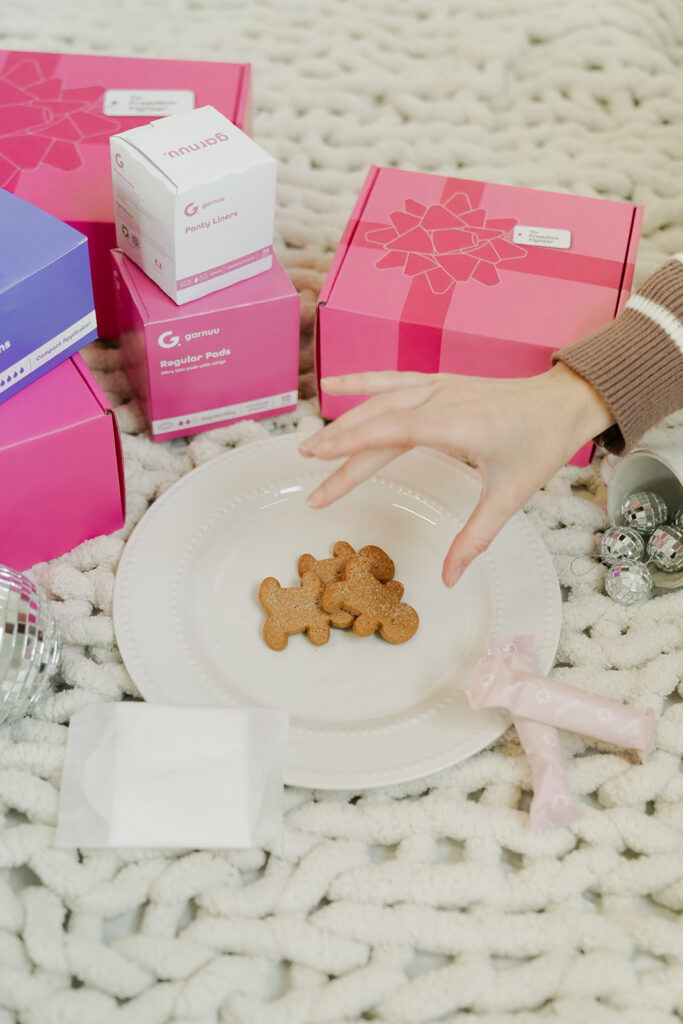 Hand reaching for cookies beside Garnuu boxes on knit blanket, festive branding photos detail.
