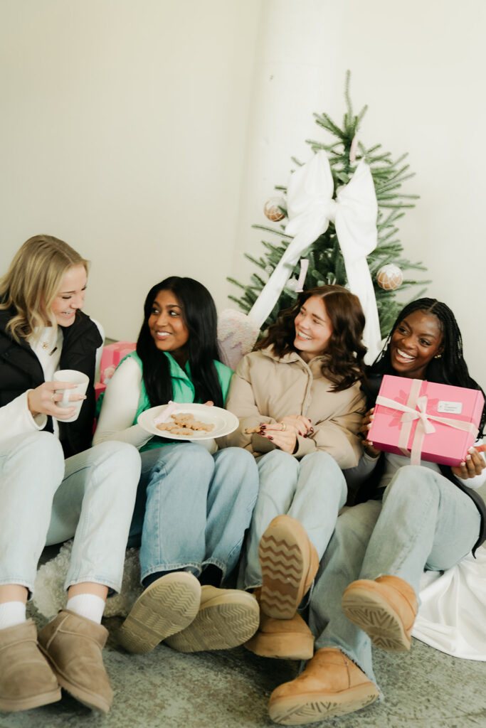 Friends laughing on floor beside tree with Garnuu gifts and cookies, human-centered branding photos.