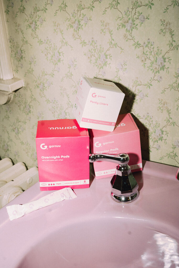 Stack of Garnuu boxes styled on a retro pink sink with floral wallpaper, colorful branding photos.
