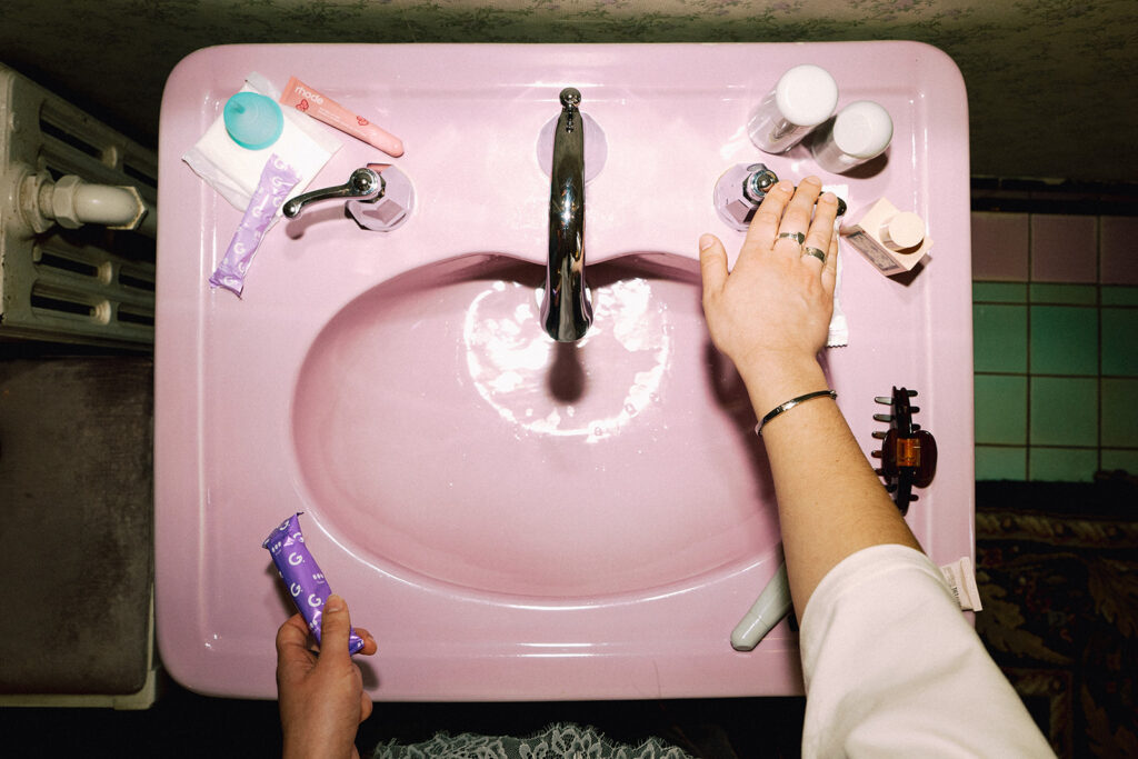 Overhead view of vintage pink sink styled with Garnuu products and hands reaching in, bold branding photos with editorial energy.