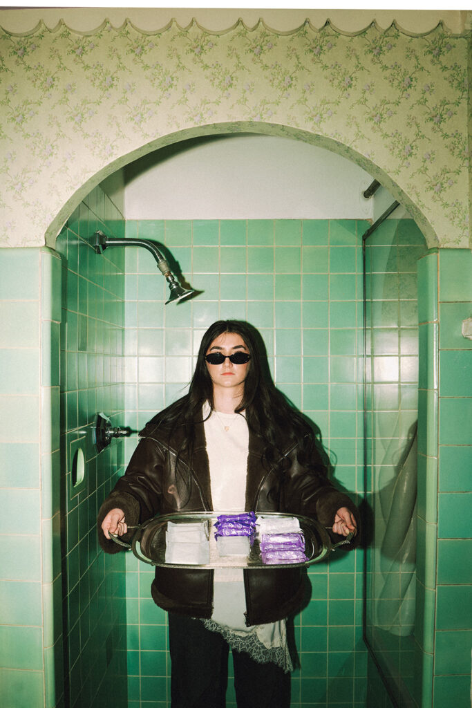 Woman in sunglasses holding silver tray of Garnuu products in mint shower, creative branding photos.