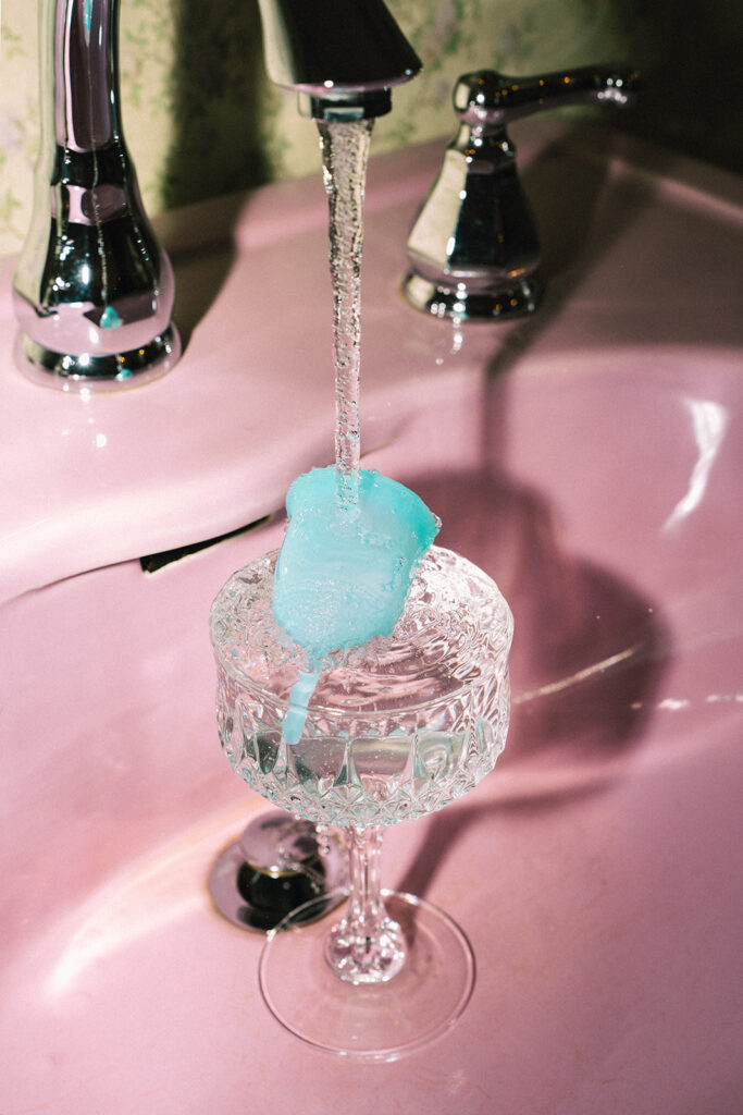 Blue Garnuu product held under running water in a glossy pink sink during creative branding photos.