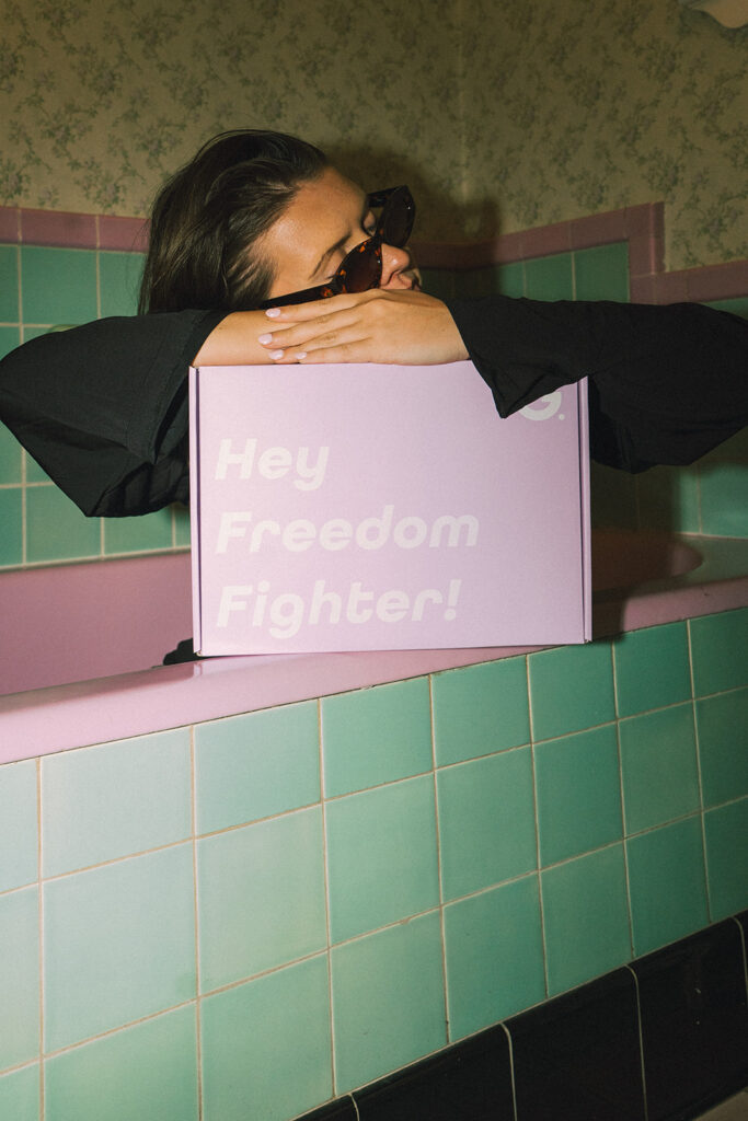 Model hugging oversized Garnuu box in retro tiled bathroom, playful brand photoshoot ideas with personality.