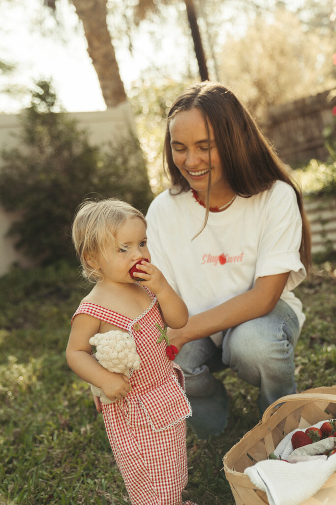 Mother and child eating strawberries in backyard sunshine, soft branding photos for Garnuu.