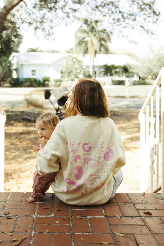Woman seated on porch with child wearing Garnuu sweatshirt, everyday lifestyle brand photoshoot imagery.