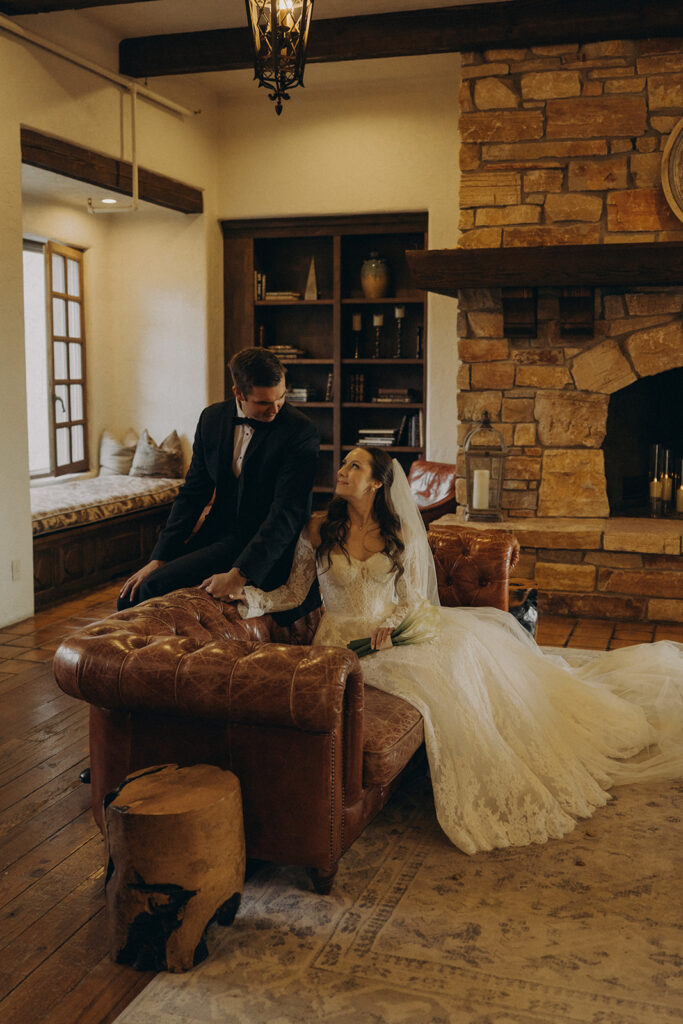 Newlyweds sit on leather couch in stately library at historic wedding venue Edward Anne Estate