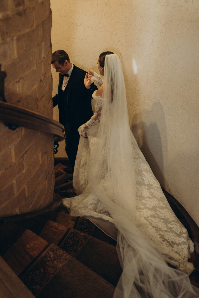 Groom chivalrously helps his bride down the curved stone steps of historic wedding venue Edward Anne Estate
