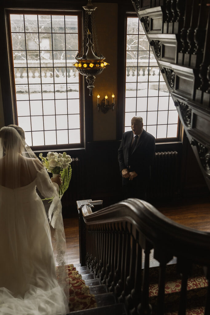Bride walks down ornate walnut steps and is met with her father's look of sheer surprise during first look